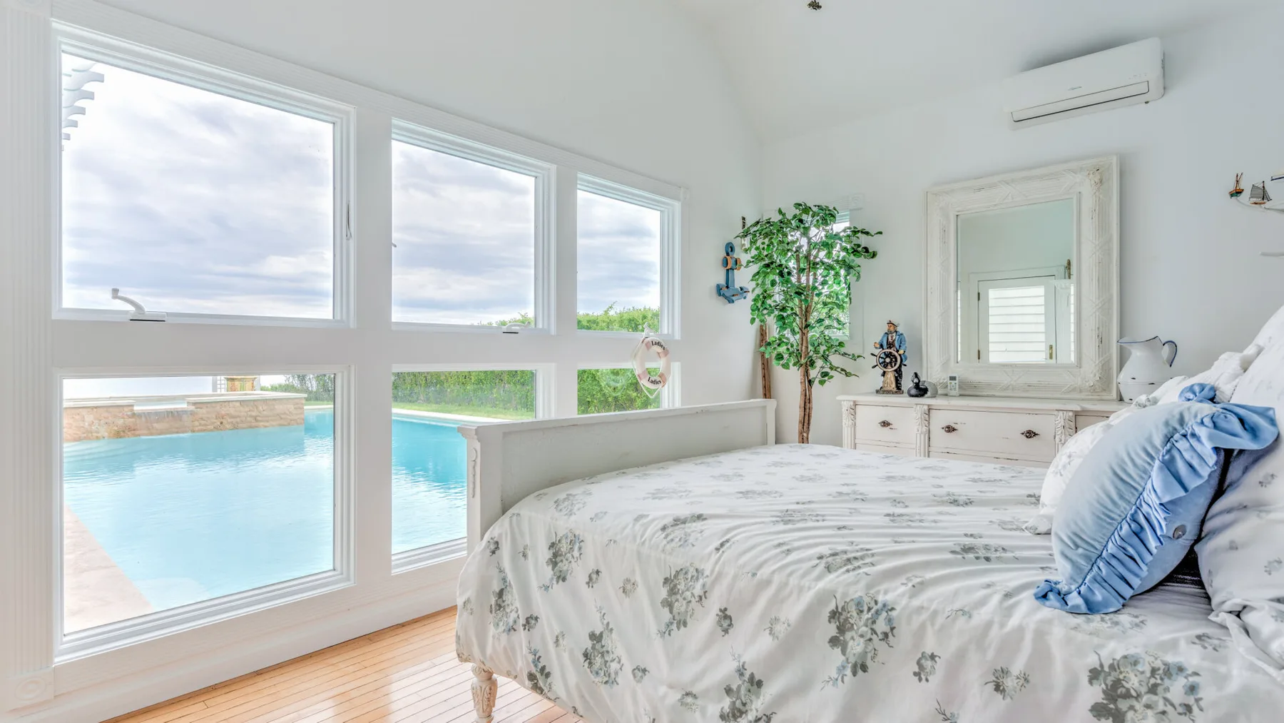 A bright bedroom with a floral bedspread and large windows overlooking a pool.