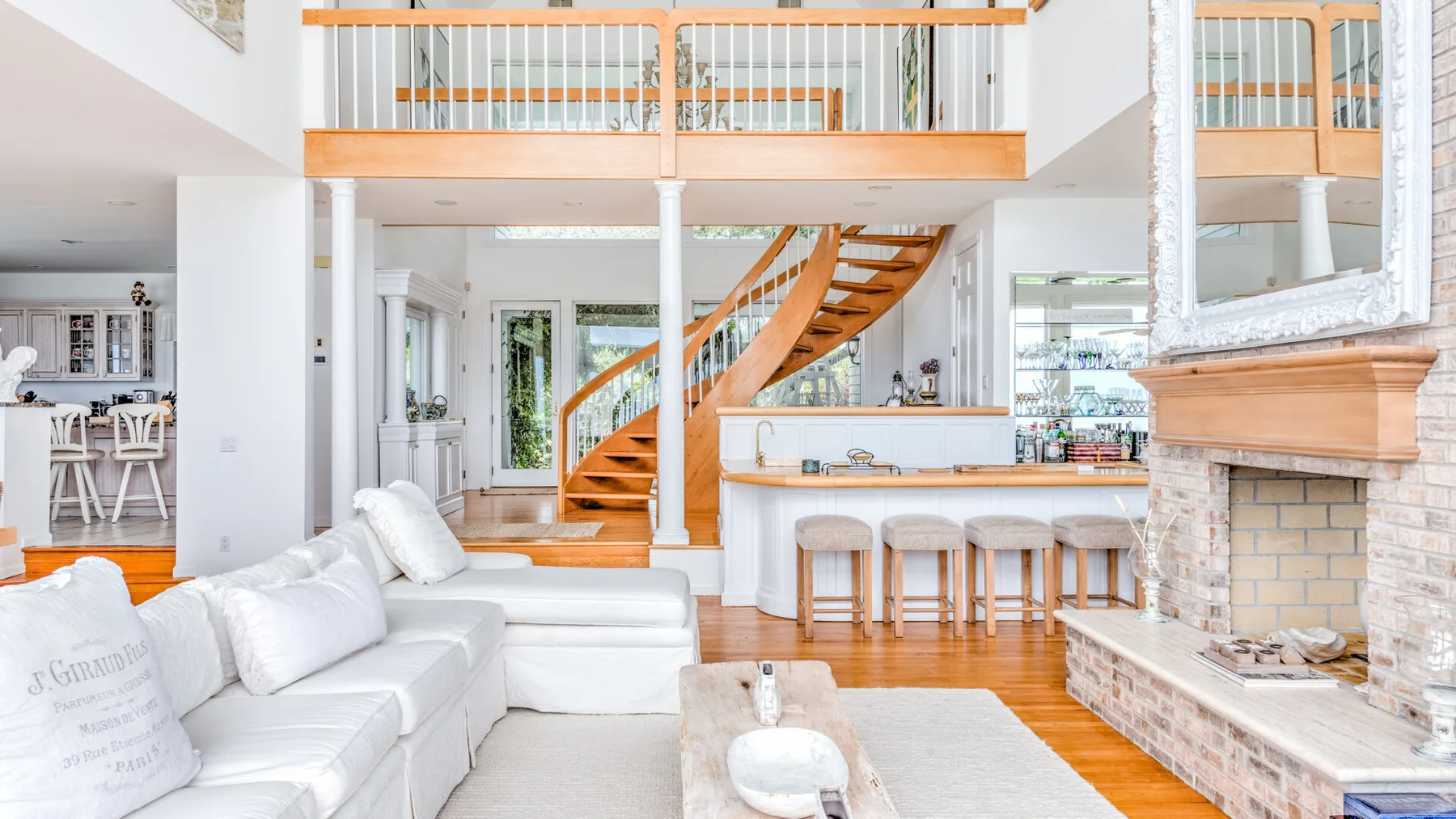 A bright living room with white seating, a central staircase, and a fireplace.