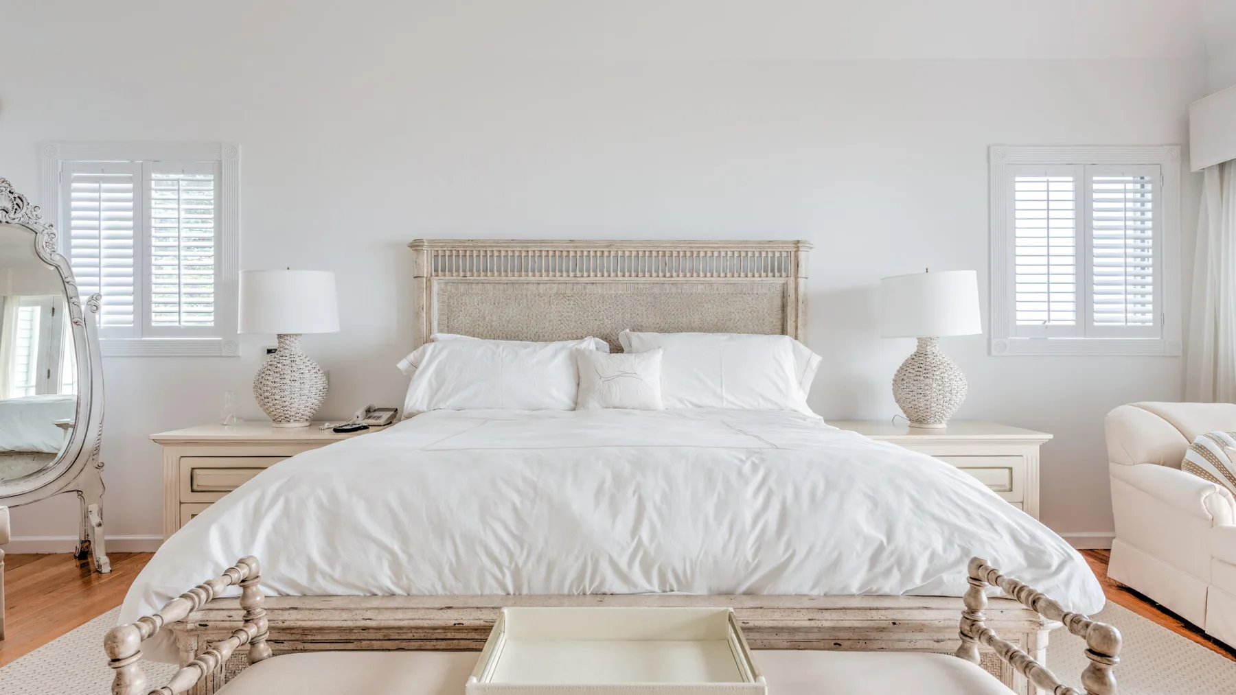 A bright bedroom with a large bed, pale bedding, and matching bedside lamps.