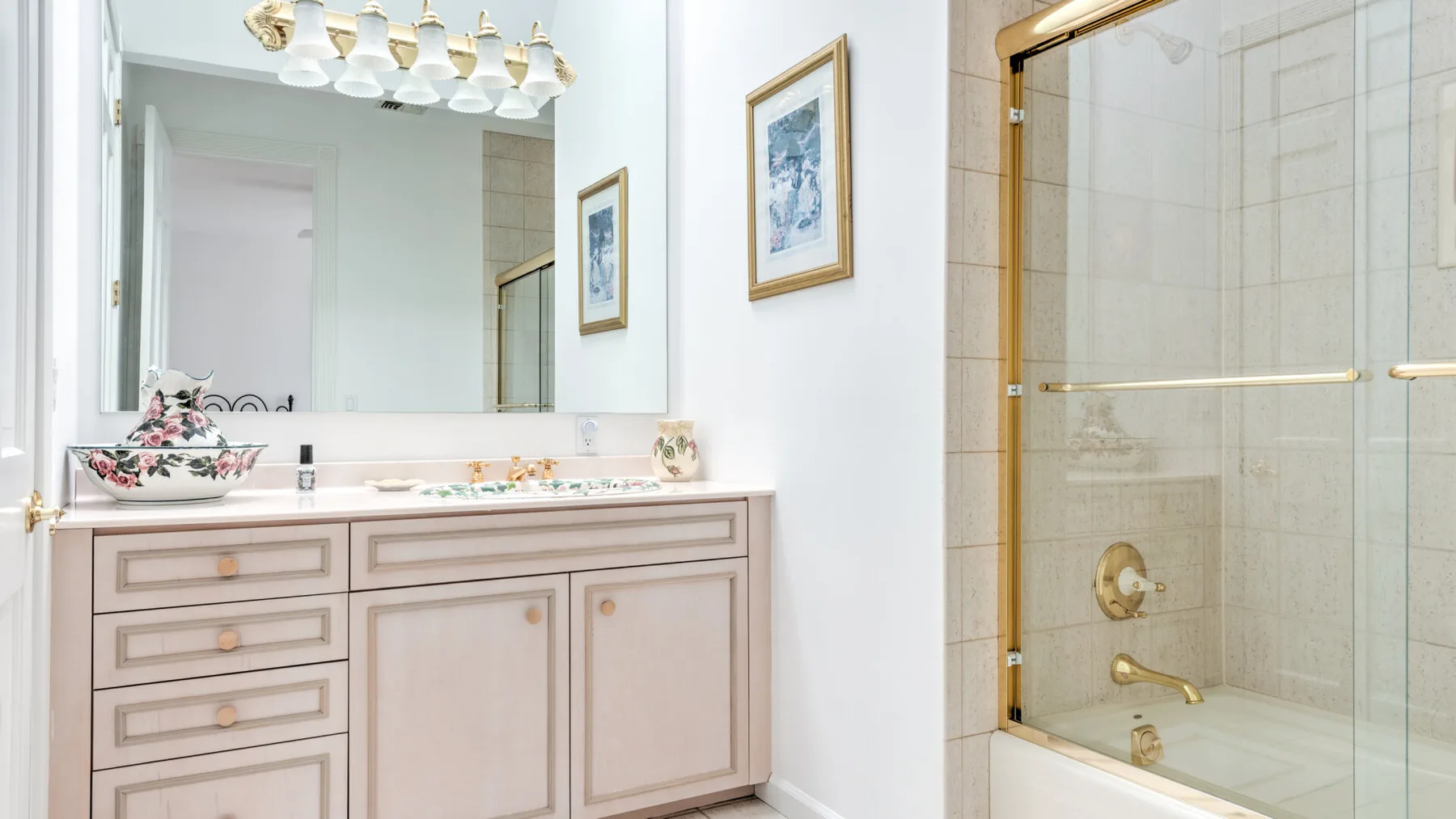 A bright bathroom with a long vanity, framed artwork, and a glass shower.