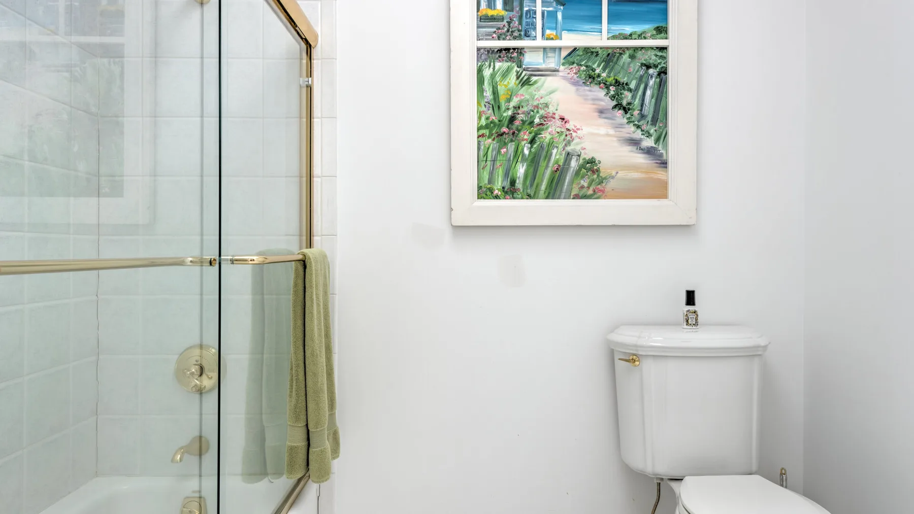 A bright bathroom with a glass shower and a framed tropical scene.