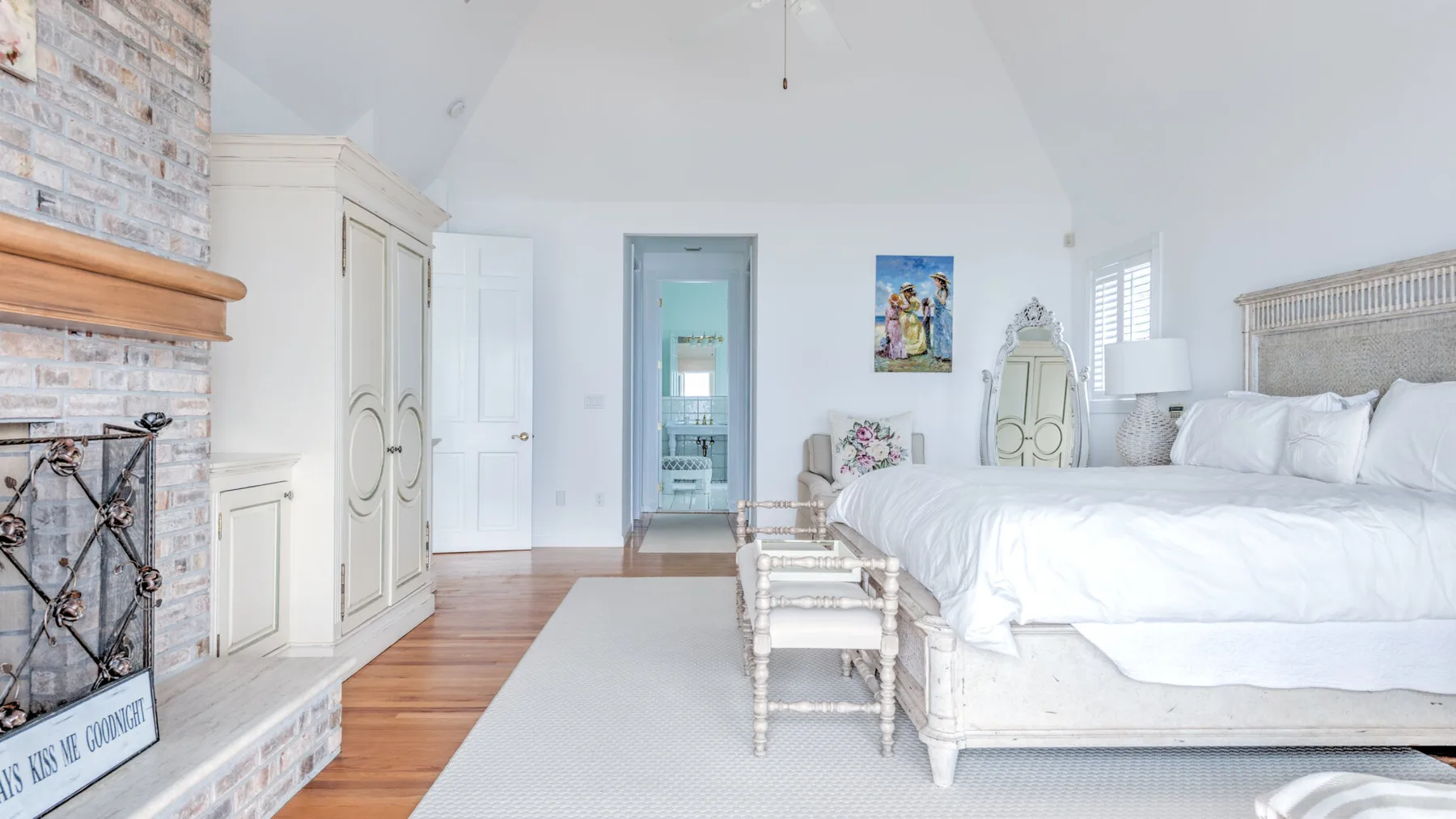 A bright bedroom with a white bed and a light rug.