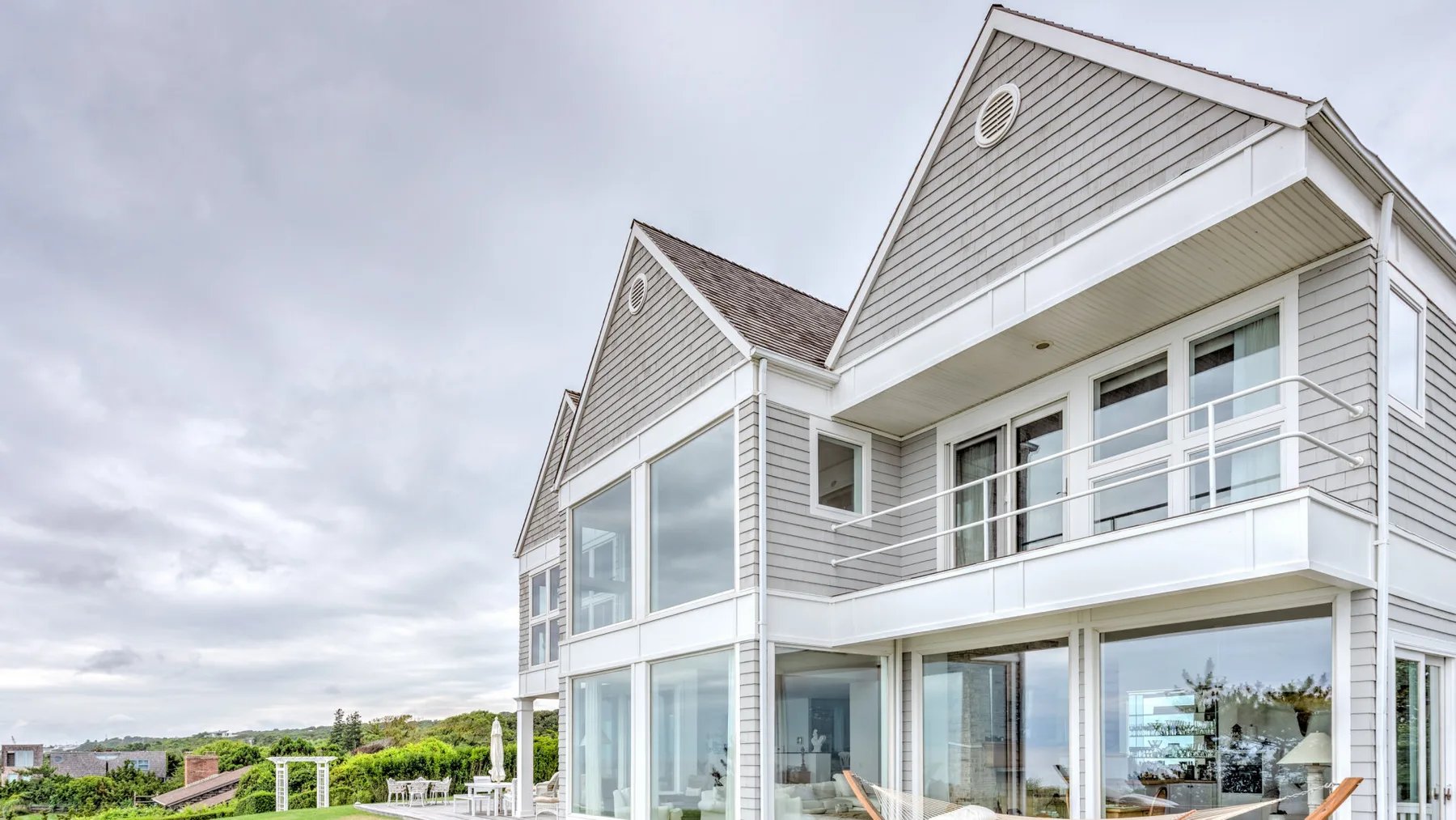 A large coastal-style house with broad windows and a balcony.
