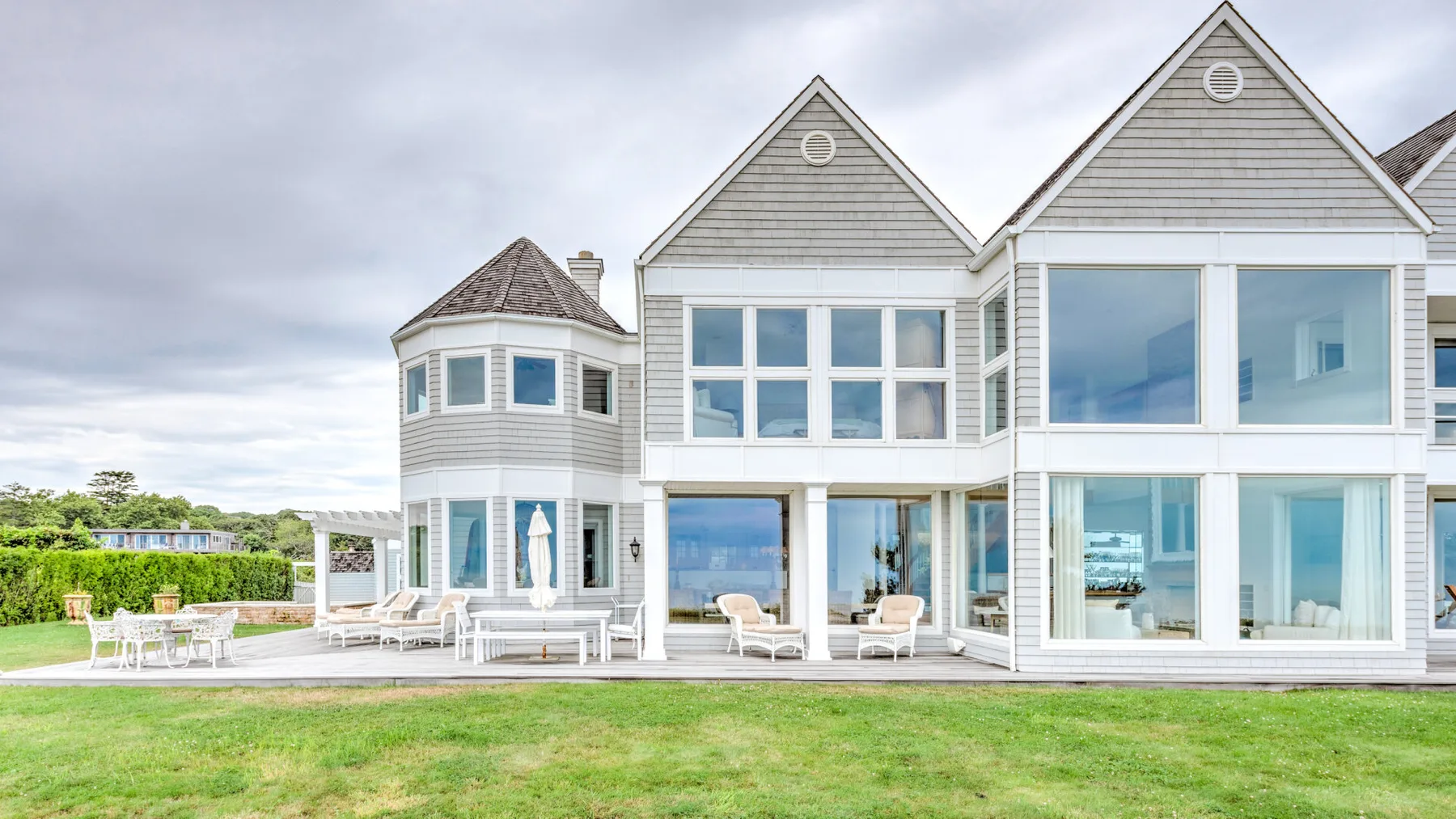 A large house with broad windows overlooks a green lawn and outdoor seating.