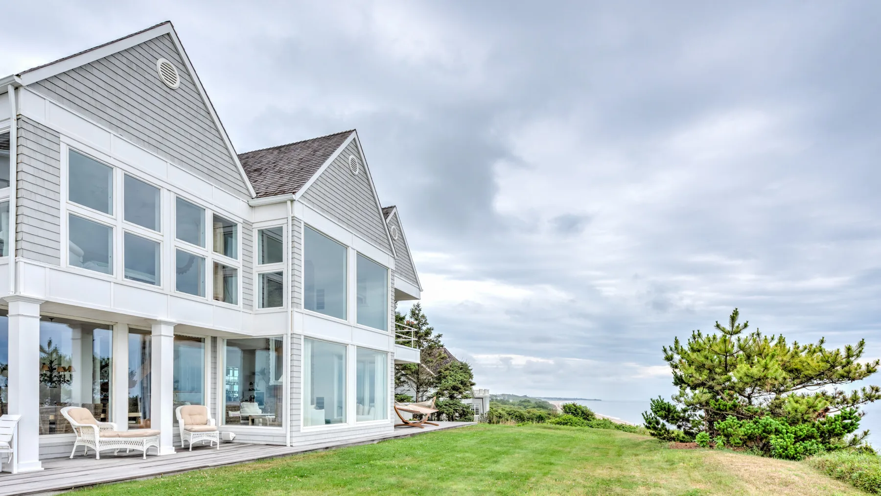 A modern house with large windows sits beside a green lawn under a cloudy sky.