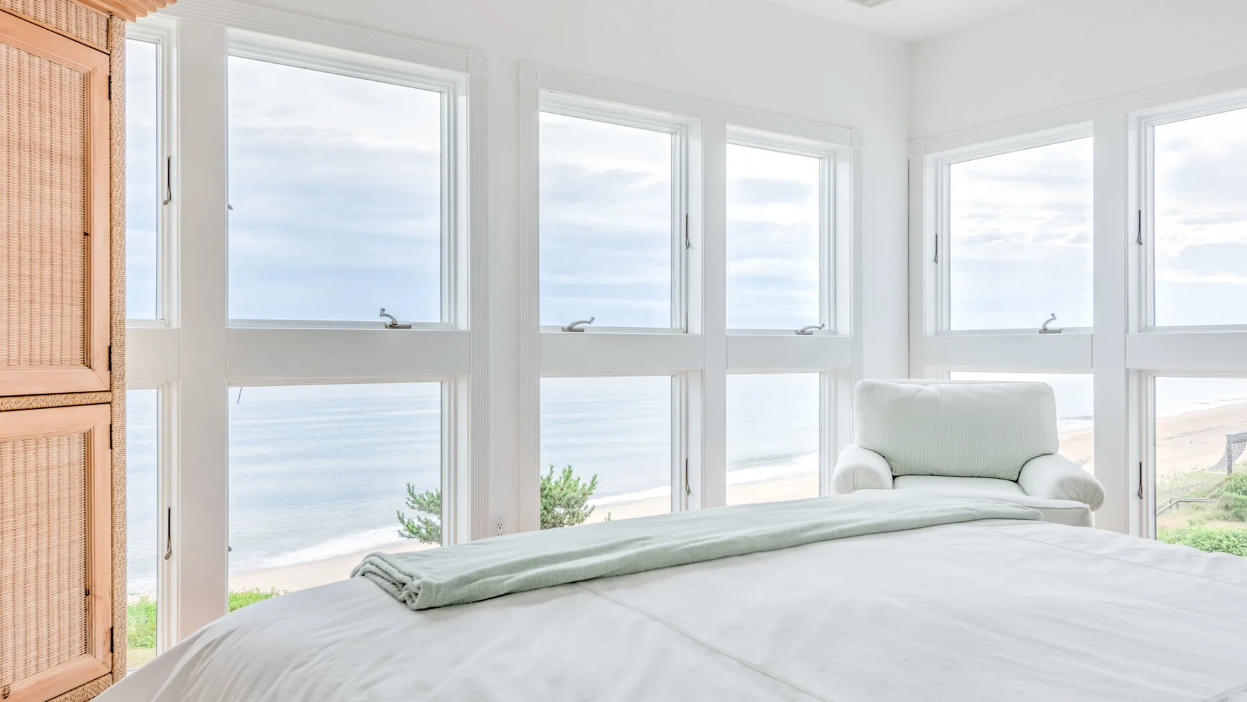 A bright bedroom with a bed beside large windows overlooking the water.