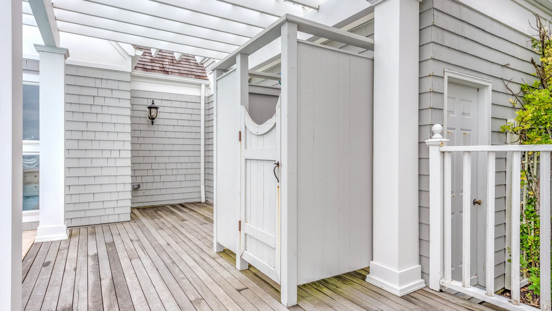 A covered outdoor deck with a white privacy screen and gray siding.