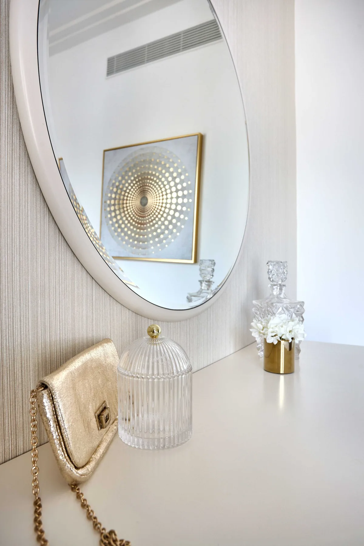Un tocador con un gran espejo ovalado, una obra decorativa y pequeños accesorios.