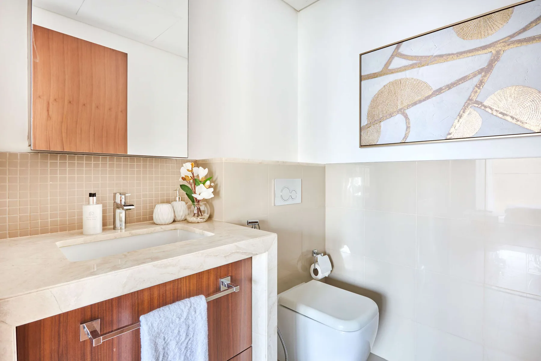Un baño con lavabo, inodoro y una obra enmarcada en la pared.