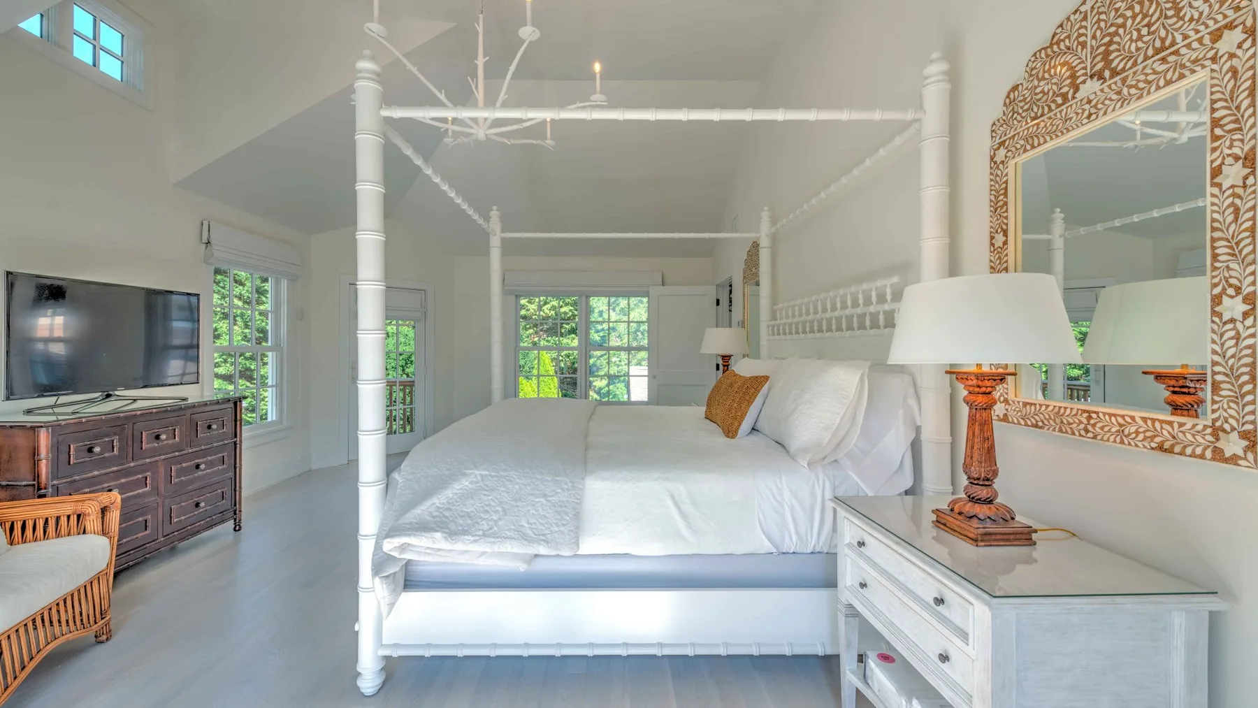 A bright bedroom with a white canopy bed and a dresser beside the window.