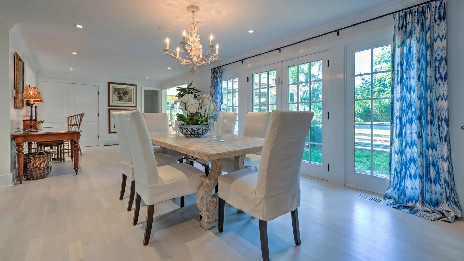 A bright dining room with a long table beside tall glass doors.