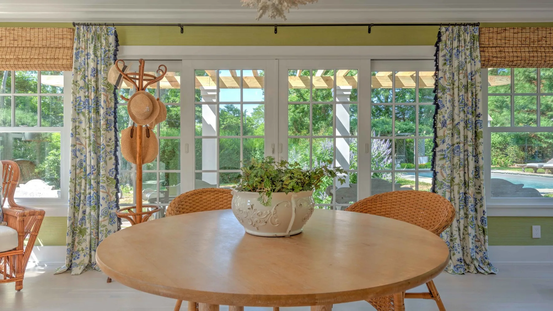 A bright dining area has a round wooden table with a potted plant.