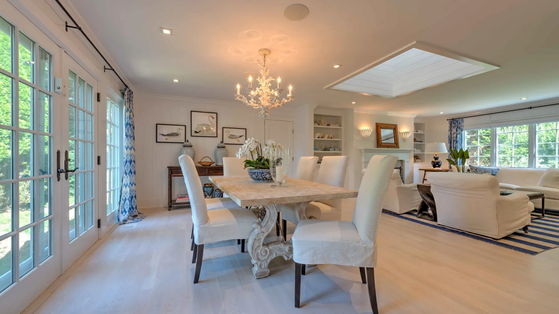 A bright open dining and living area features a long table and large windows.
