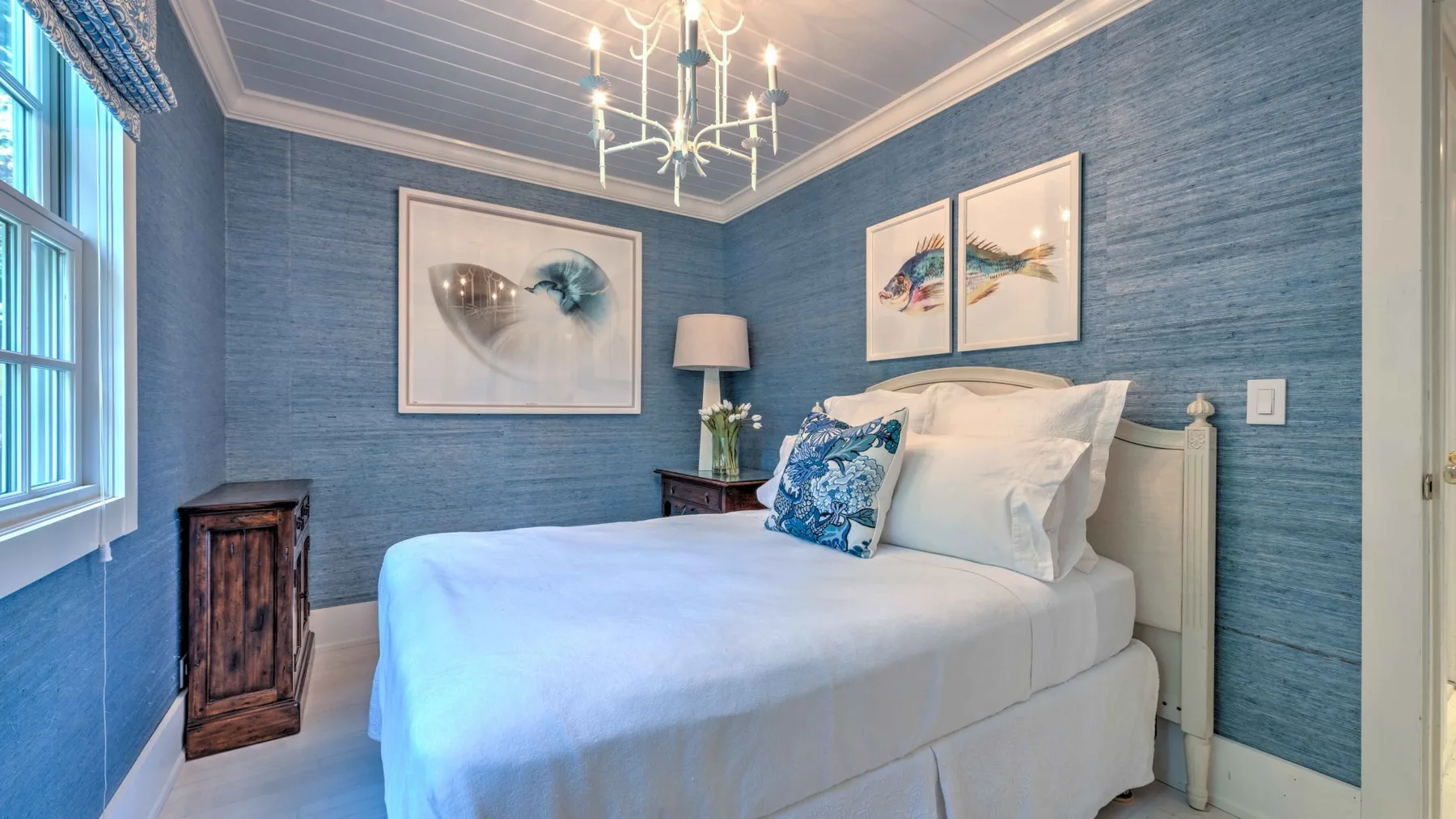A bedroom with a white bed, blue walls, and framed artwork.