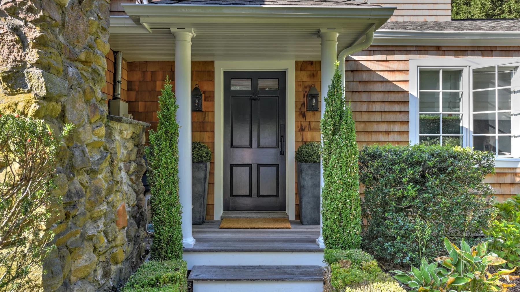 A house entrance with a dark front door, porch, and surrounding shrubs.