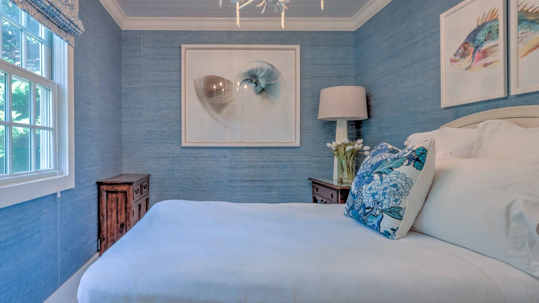 A bedroom with a white bed, blue walls, and framed artwork.
