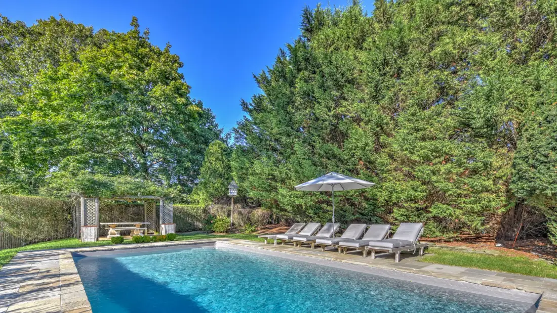 An outdoor swimming pool is surrounded by lounge seating and trees.
