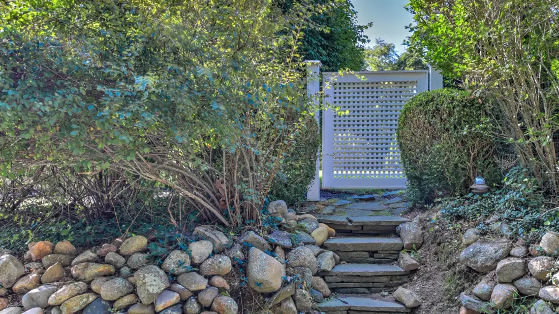 A garden path with stone steps leads to a white lattice gate among greenery.