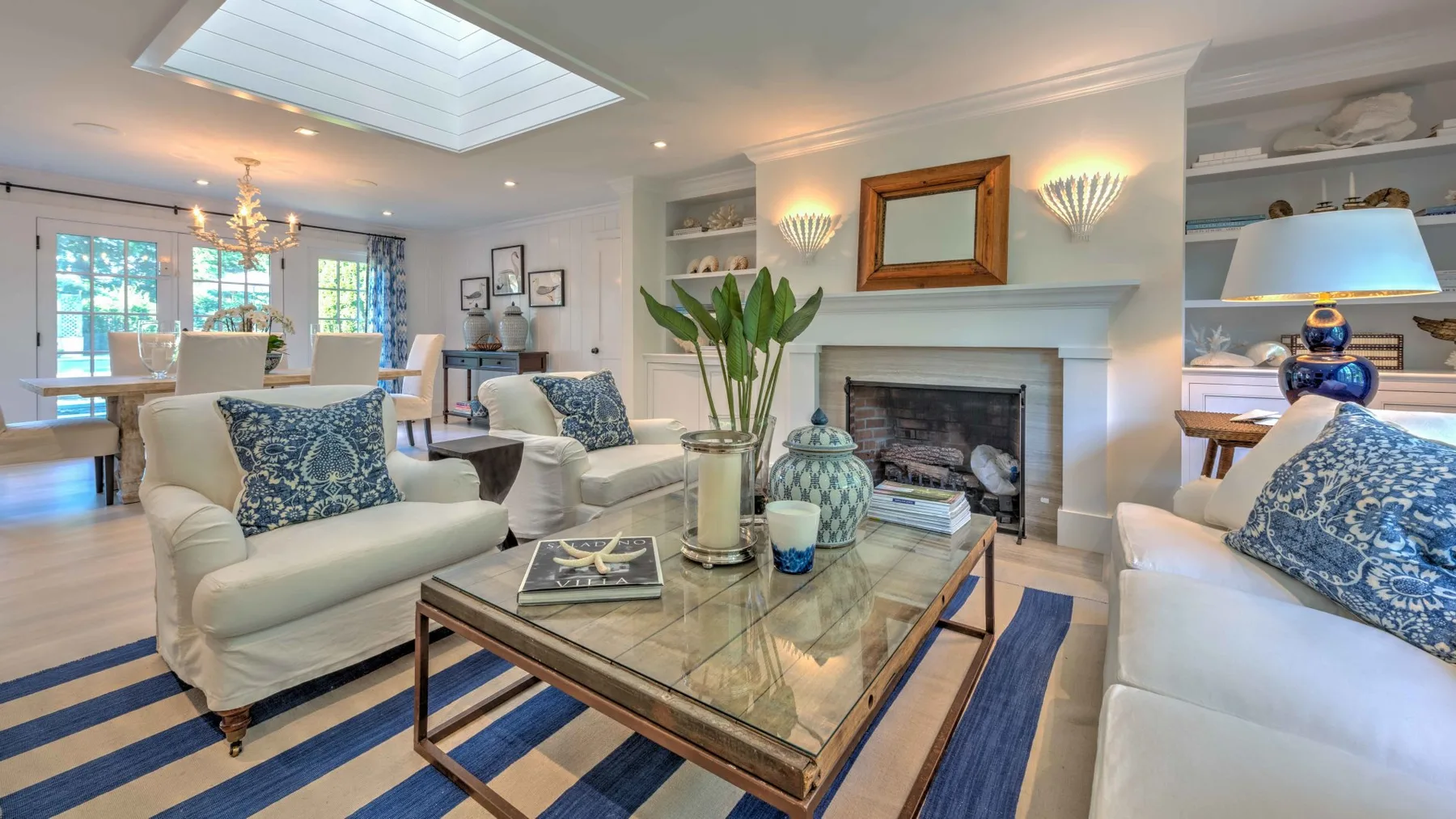 A bright living room with seating arranged around a glass coffee table and fireplace.