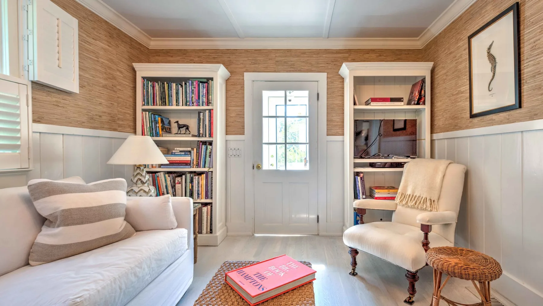 A bright sitting room with cushioned seating, bookshelves, and a central window.