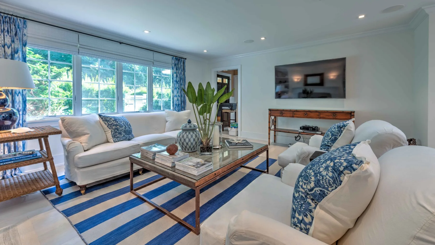 A bright living room with white seating, a coffee table, and large windows.