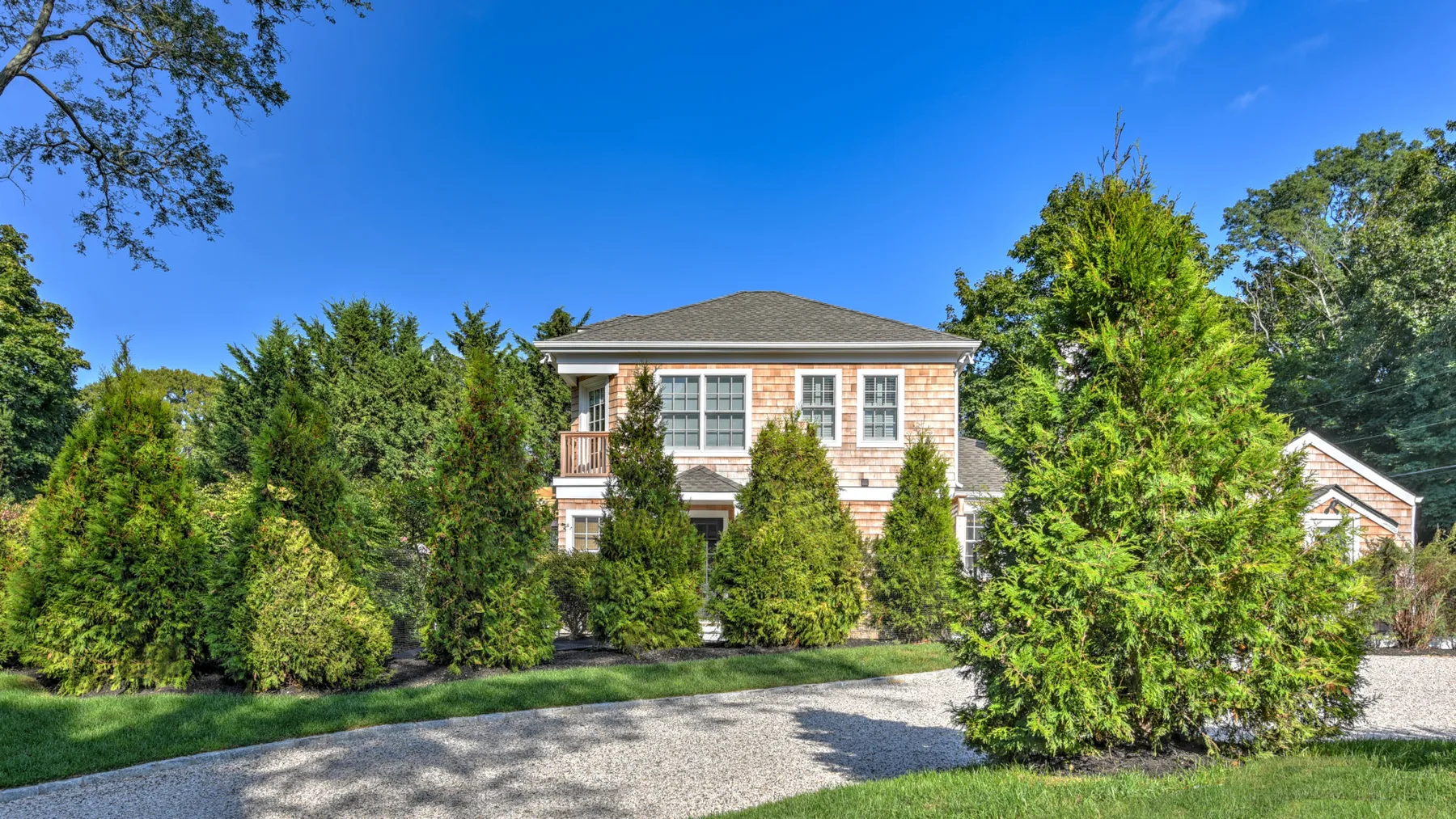 A two-story house stands behind trees beside a curved gravel driveway.