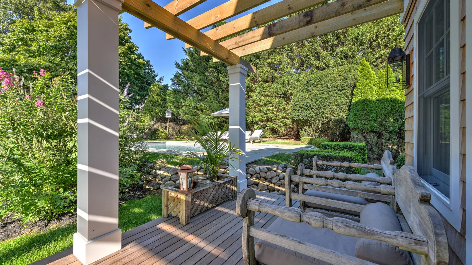 A covered outdoor seating area overlooks a garden and swimming pool.