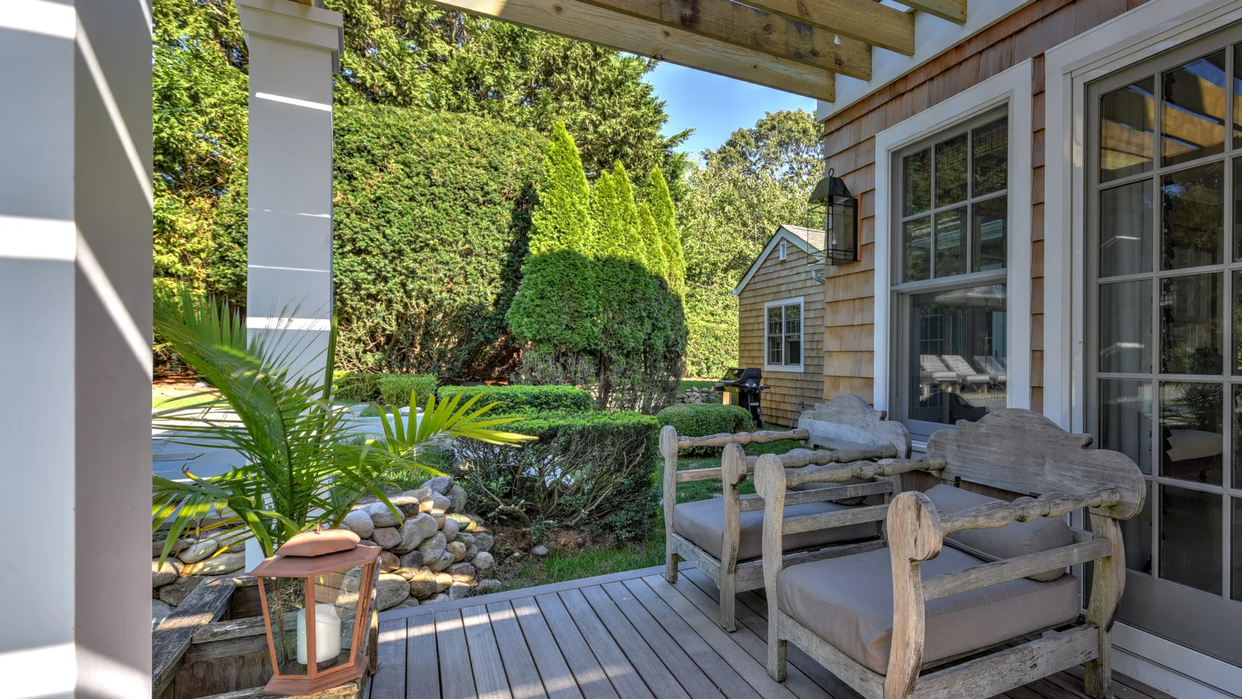A covered patio with outdoor seating overlooks a landscaped garden.