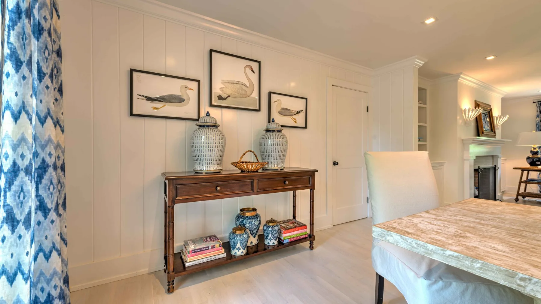 A dining area with a wooden console table, framed bird prints, and a table in the foreground.
