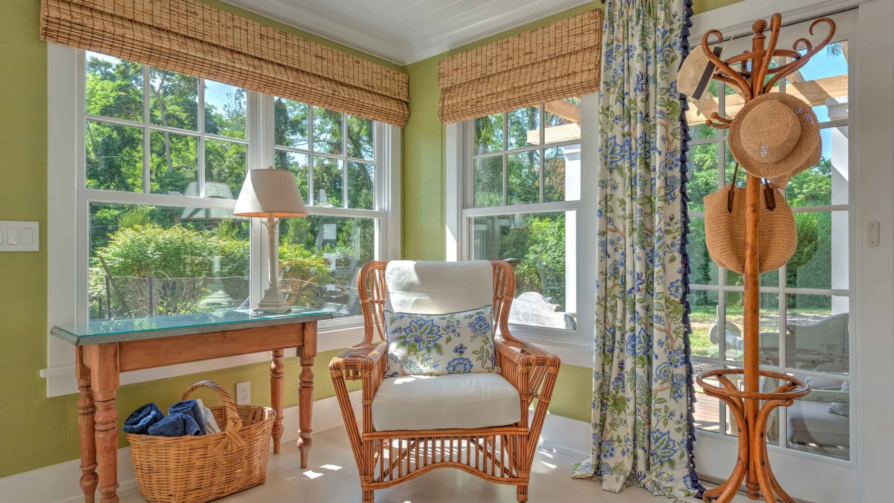 A bright sitting area with wicker seating, large windows, and a floral curtain.