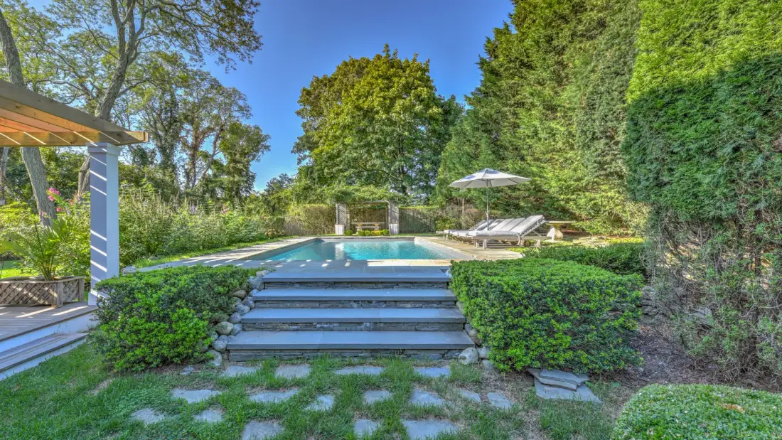 An outdoor swimming pool sits beyond broad steps in a landscaped garden.