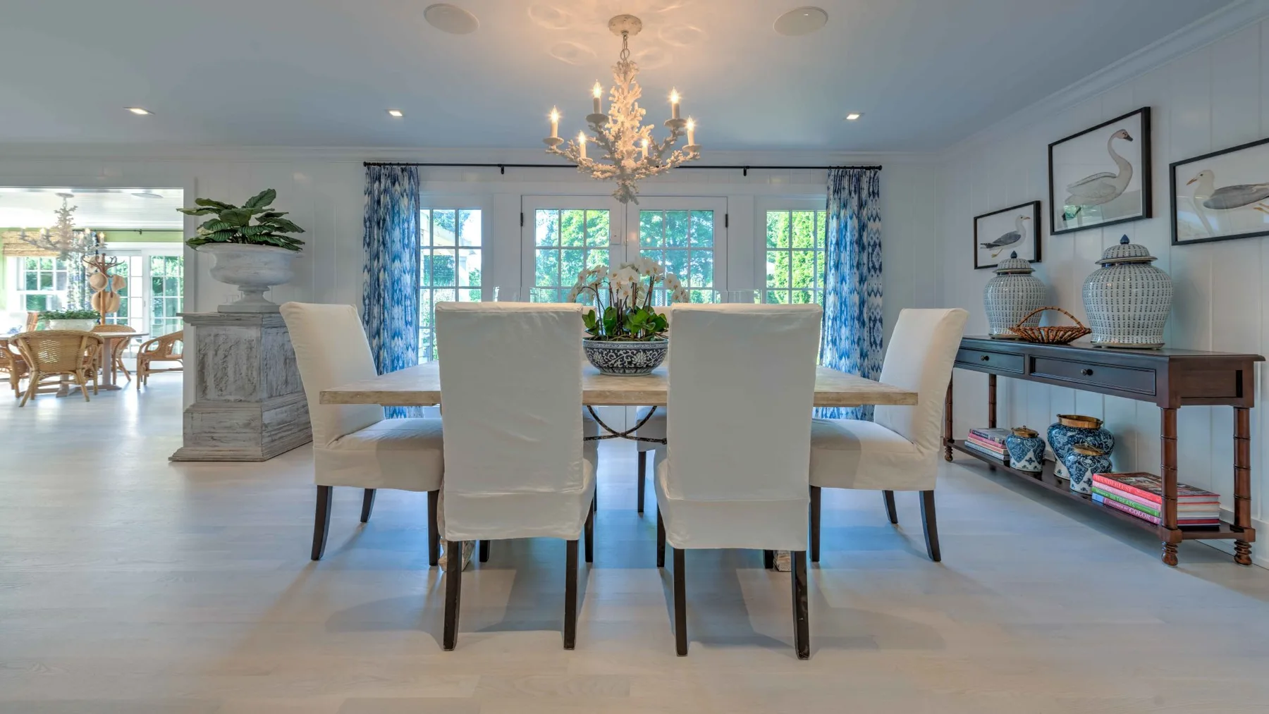 A bright dining room with a long table, upholstered seating, and a chandelier.