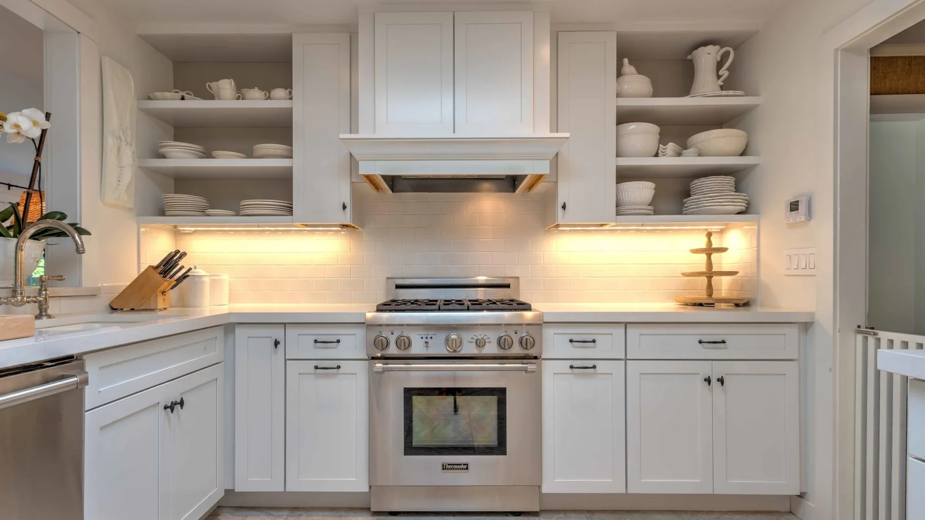 A bright kitchen with white cabinetry, open shelves, and a stainless steel range.