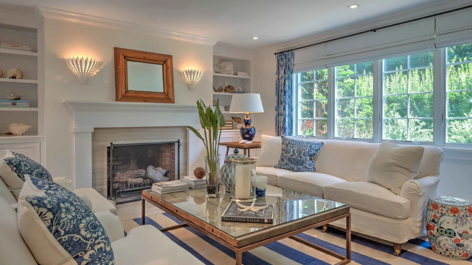 A bright living room with seating arranged around a glass-topped coffee table and fireplace.