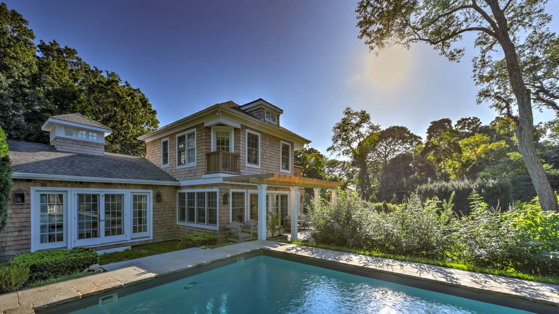A large house overlooks a swimming pool surrounded by greenery.