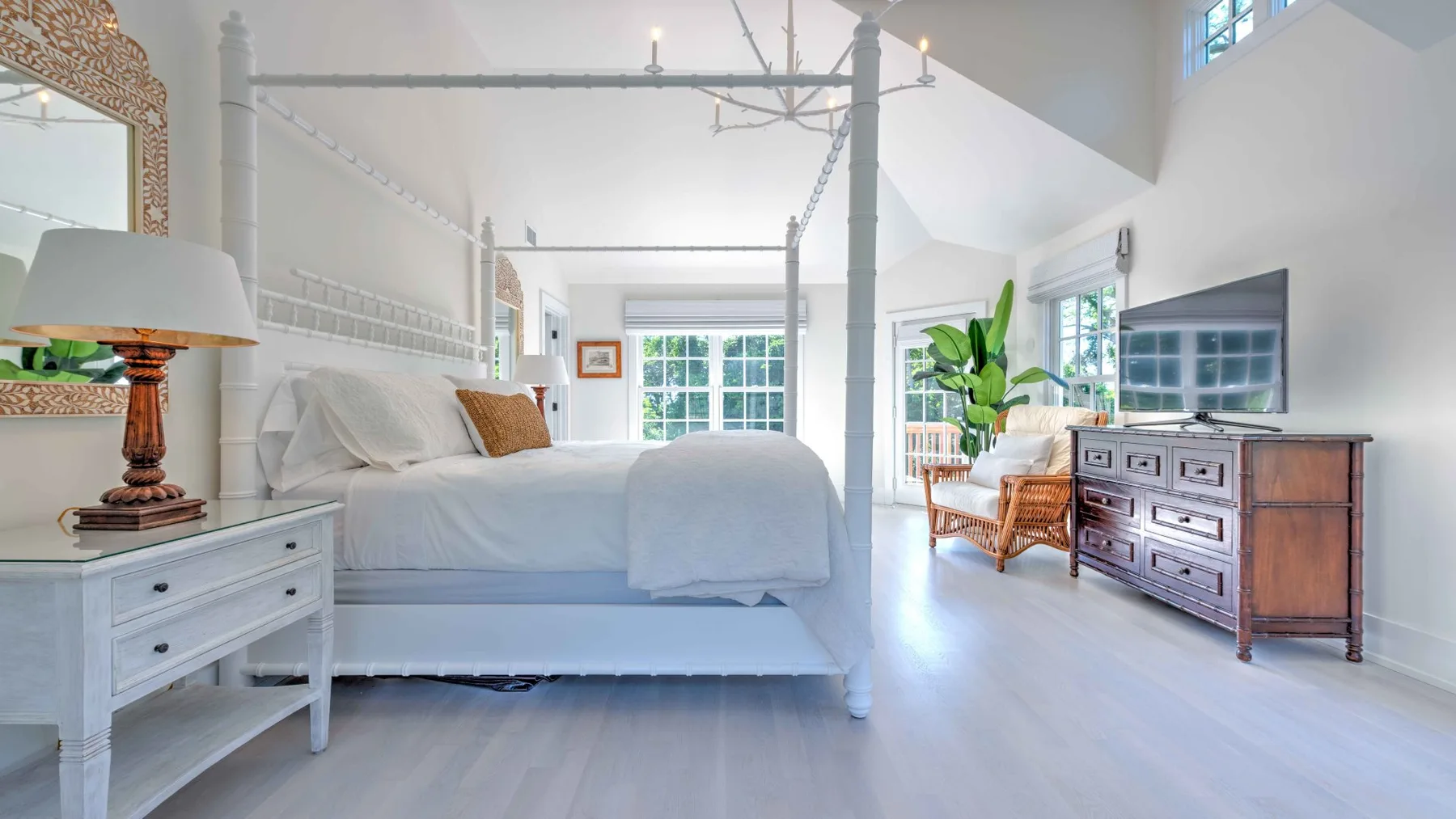 A bright bedroom with a large bed and a wooden dresser beneath a wall-mounted television.