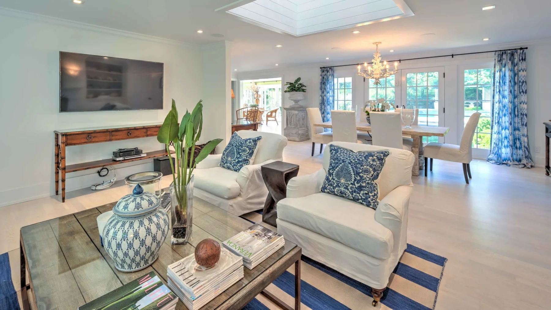 A bright open-plan living and dining area with white seating and large windows.
