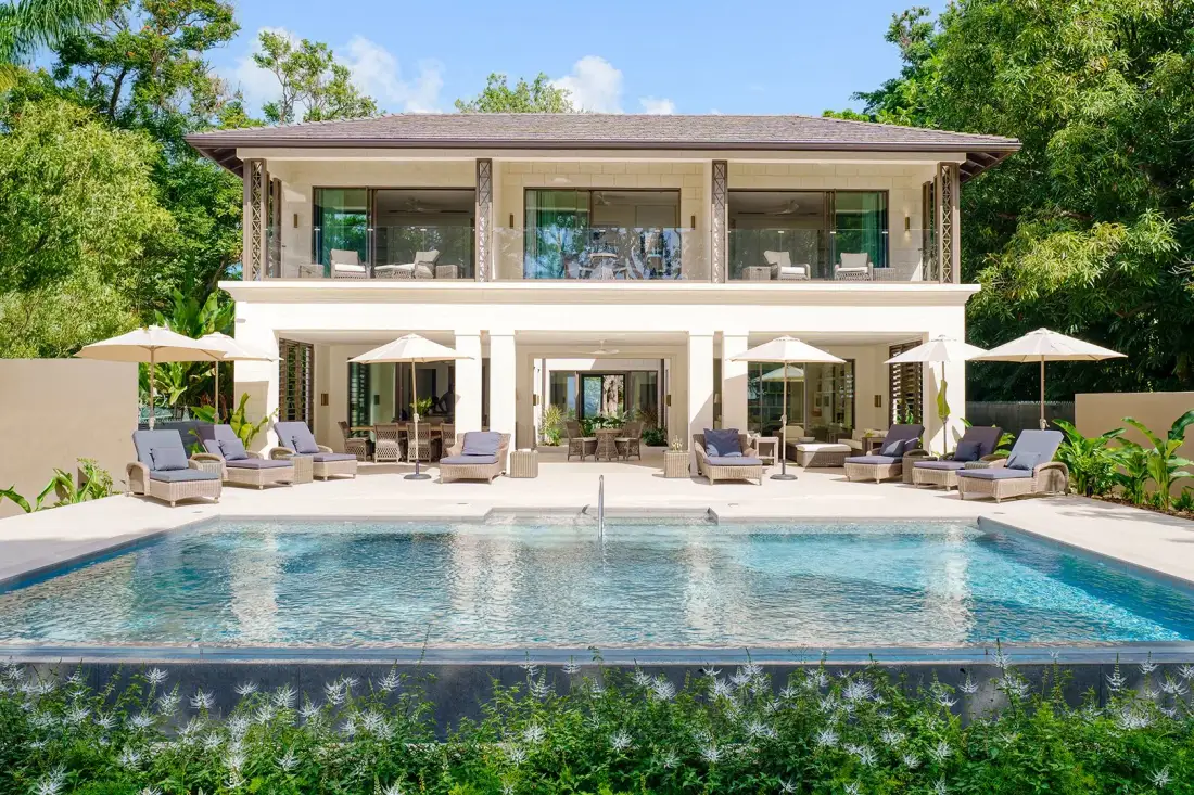 A two-story house overlooks a swimming pool, with outdoor seating and umbrellas.