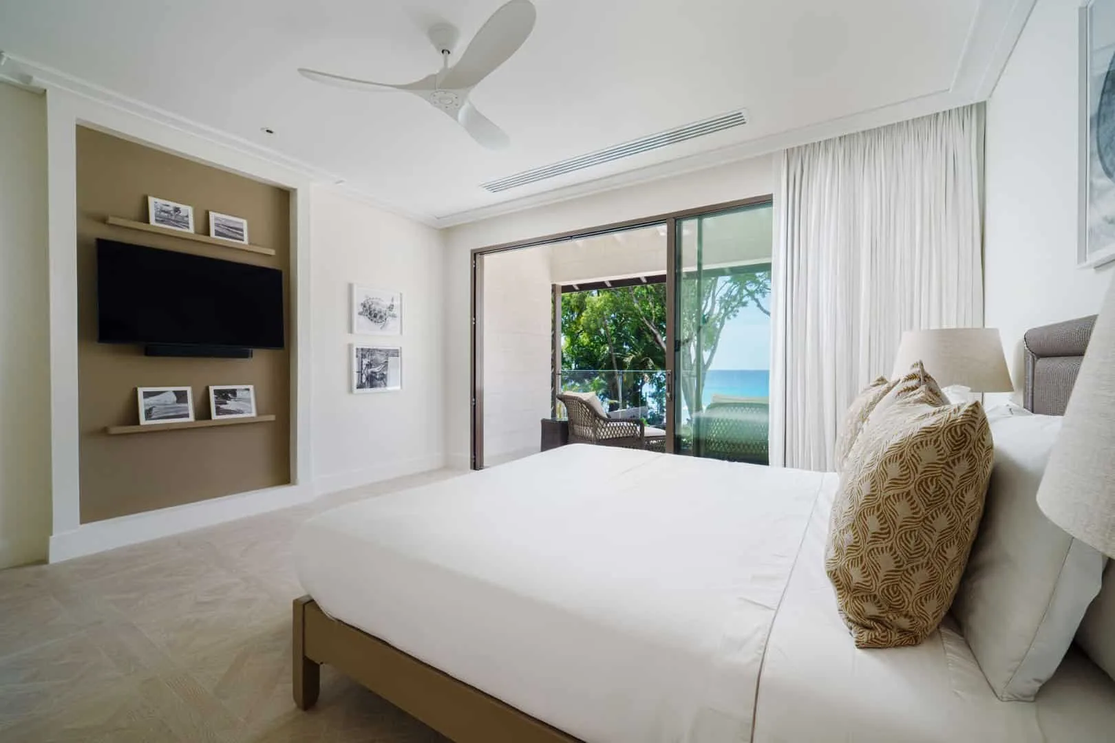 A bright bedroom with a large bed facing sliding glass doors and a leafy view.