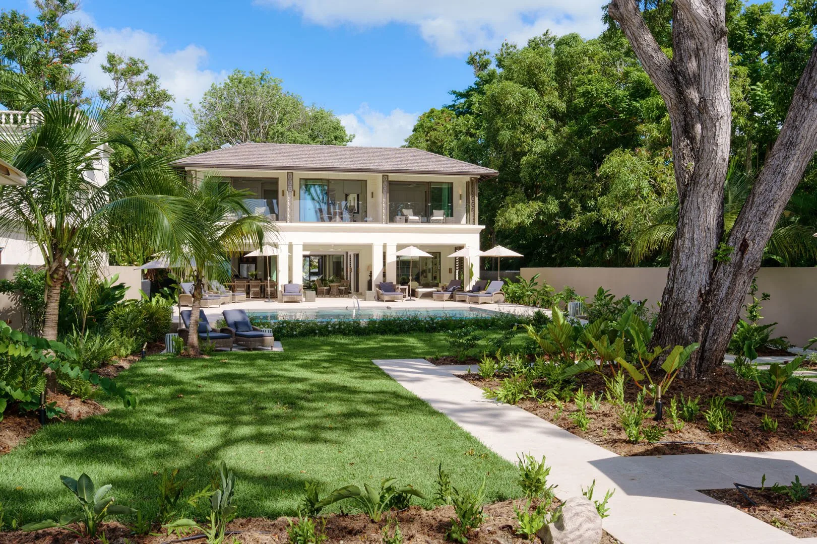 A landscaped garden path leads toward a two-story house with a pool.