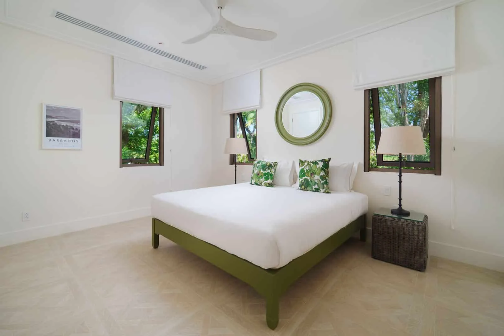 A bright bedroom with a white bed, green accents, and windows overlooking trees.