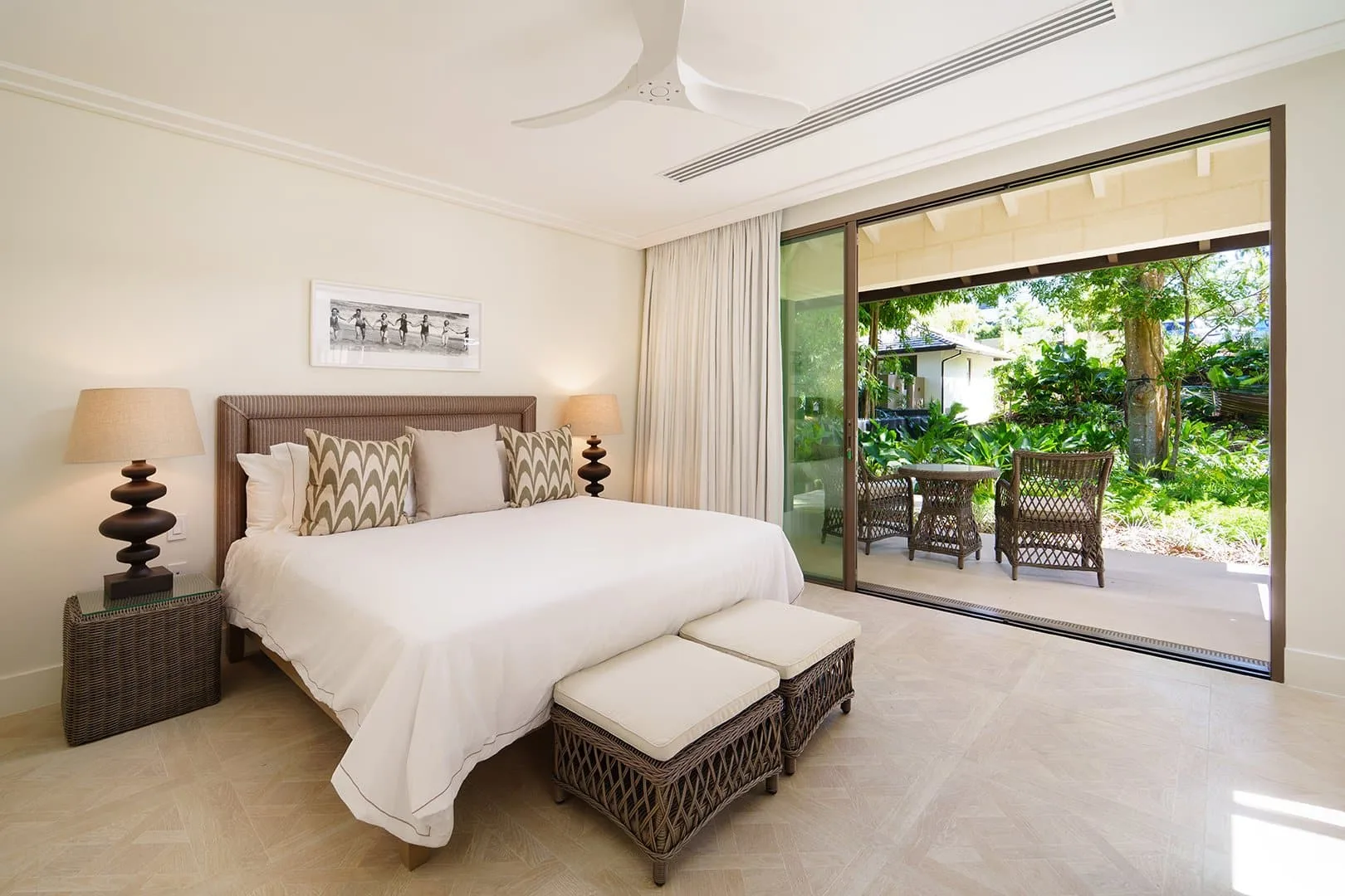 A bright bedroom with a large bed beside sliding glass doors opening onto a garden patio.