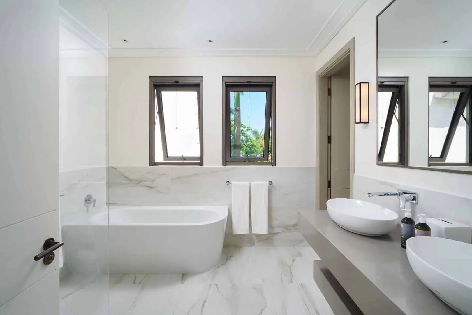 A bright bathroom with a bathtub, two sinks, and windows.