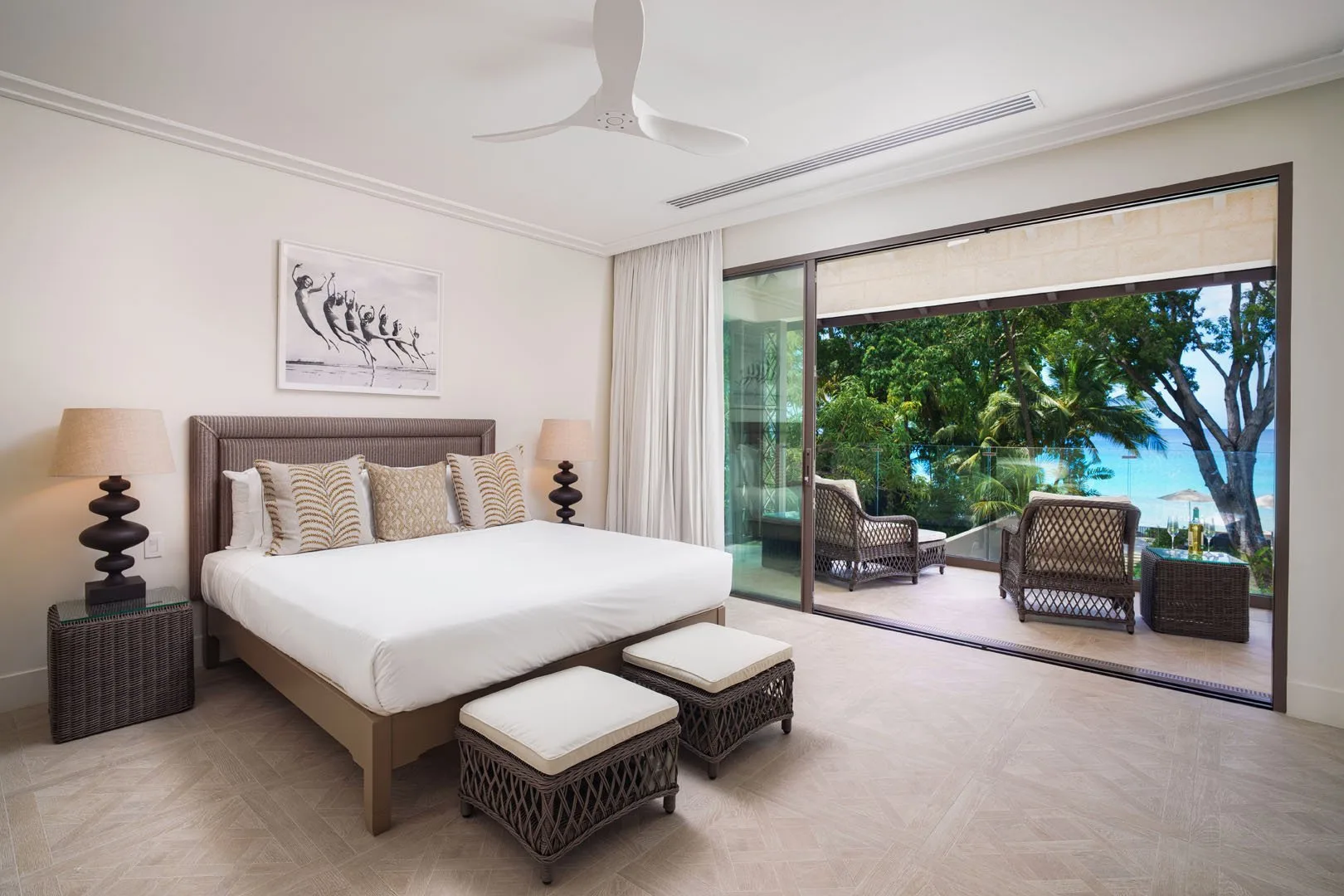 A bedroom opens onto a terrace with seating and views of greenery and water.