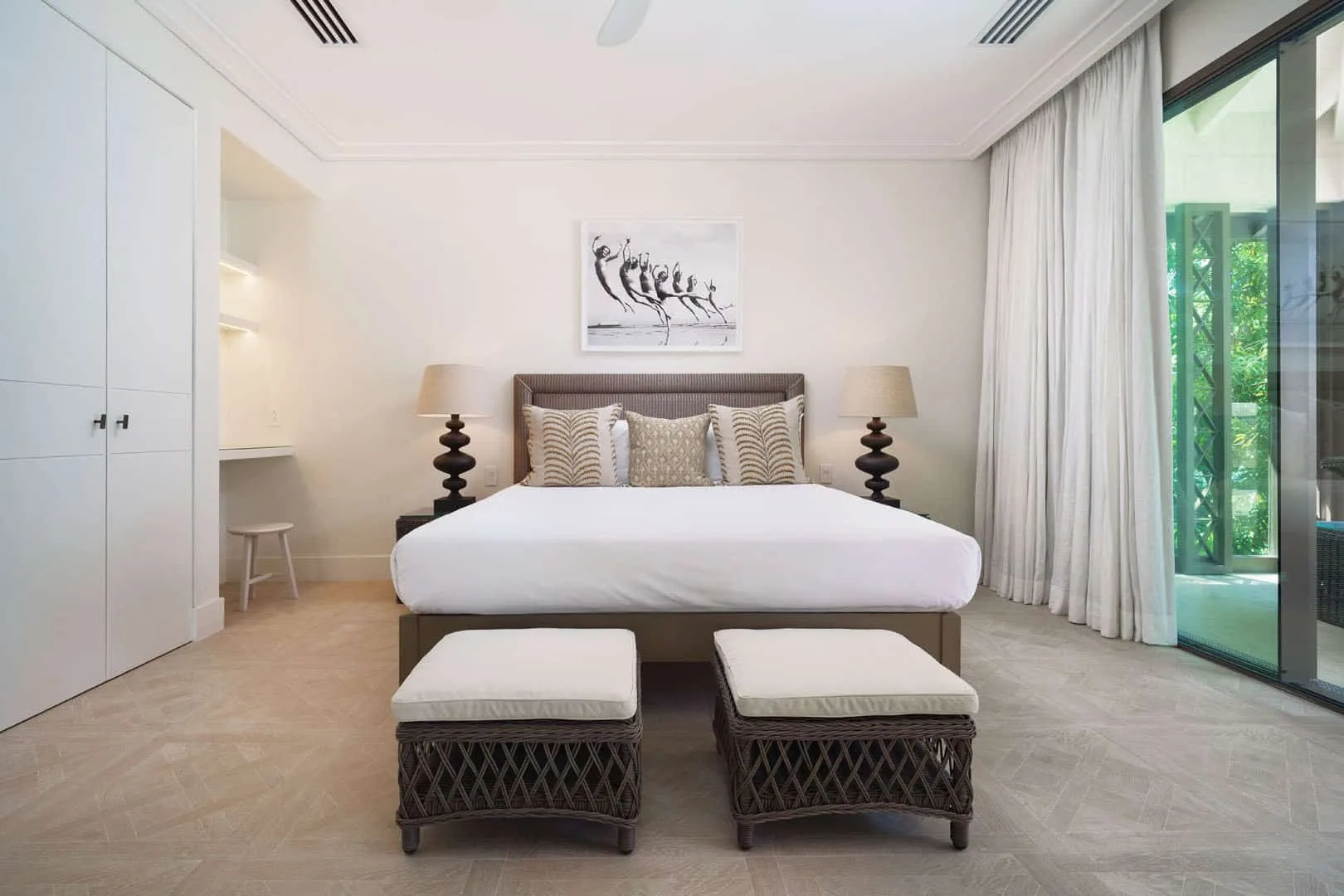 A bright bedroom with a bed, two stools, and glass doors opening to greenery.