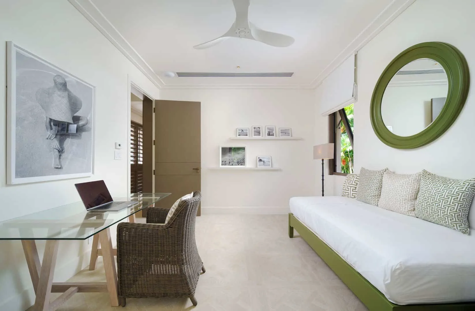 A bright bedroom with a white bed, green accents, and a glass desk.