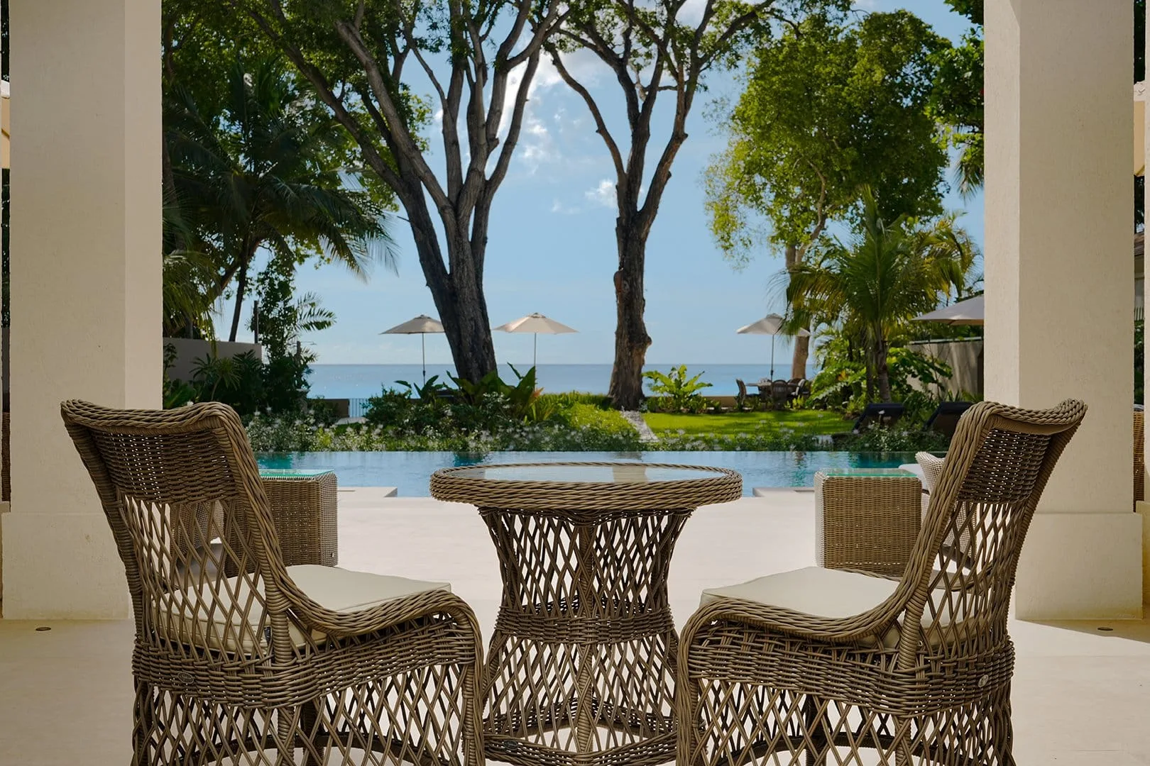 Outdoor seating overlooks a pool, with trees and the sea beyond.