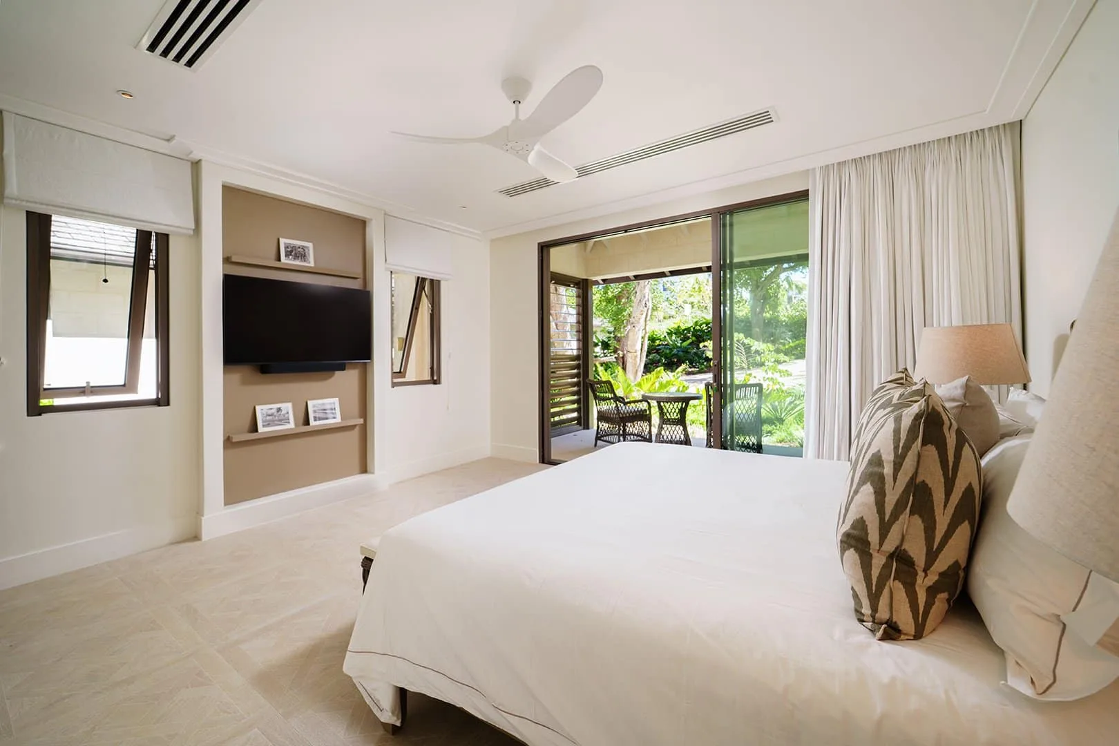 A bright bedroom with a large bed facing sliding glass doors and greenery.
