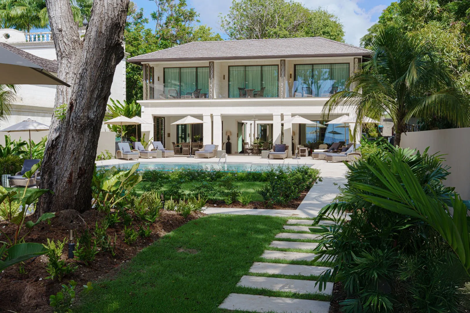 A two-story house faces a garden path, with patio seating and a swimming pool.