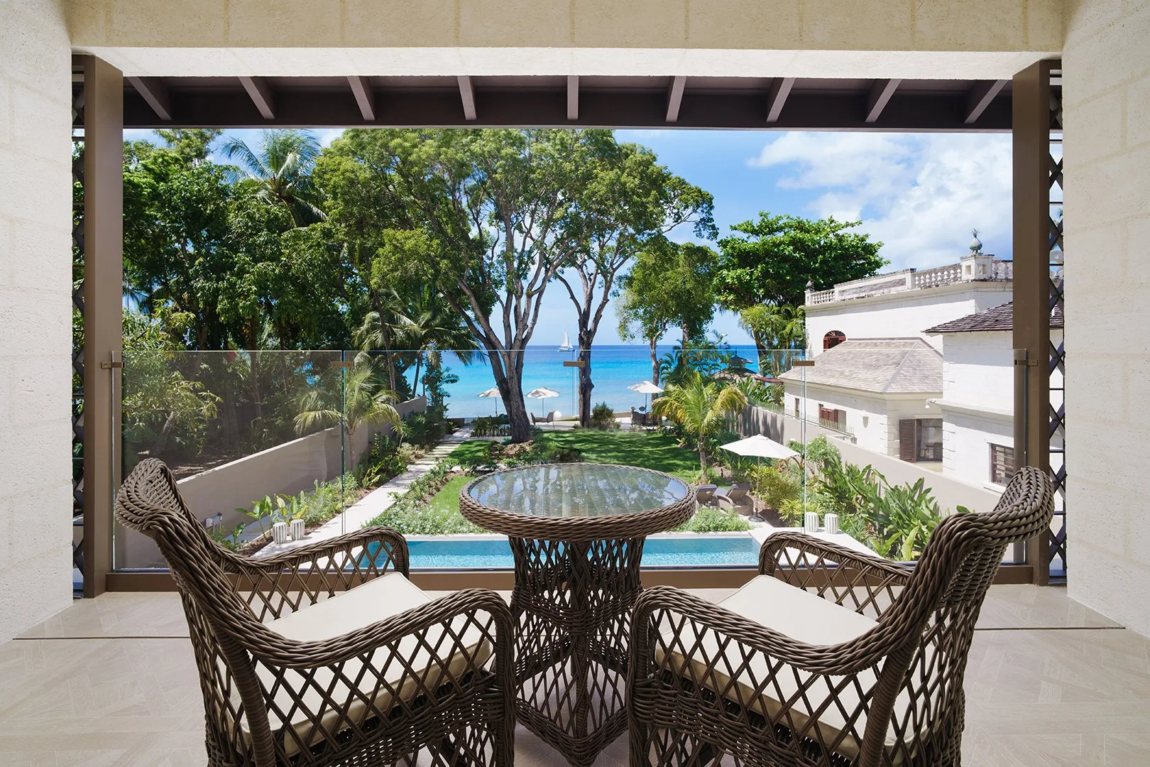 A patio seating area overlooks a swimming pool, trees, and the ocean.